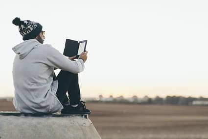 Un jeune assis face au lever du soleil avec un livre en main